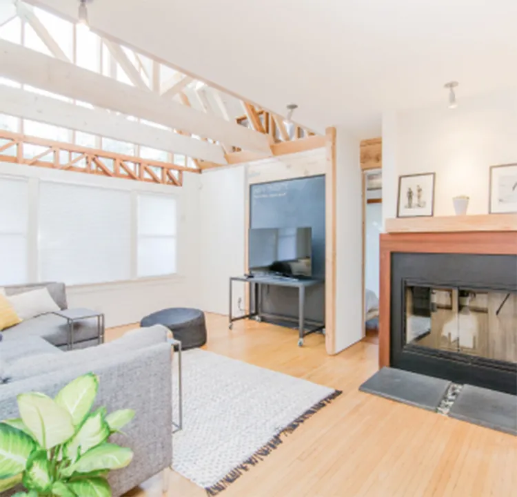天井の梁が見える明るいリビングルーム。暖炉とモダンな家具が置かれた開放的な空間